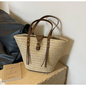 Detail of hand-woven straw tote bag with brown leather straps and gold buckle
