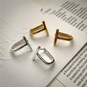 Detailed view of polished gold and silver T-shaped geometric hoop earrings on paper