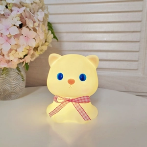 Close-up of a glowing cat night light with a red bow tie in a cozy home setting
