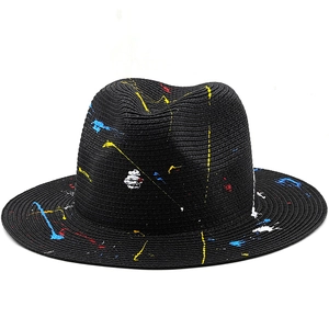 Close-up of black straw fedora with colorful graffiti paint splatters and woven texture