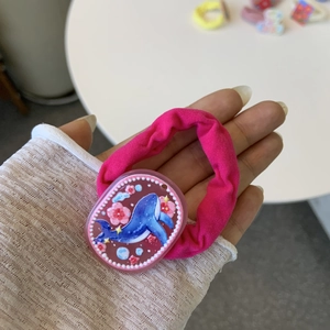 Close-up of pink fabric hair tie featuring a round resin charm with blue whale and flower