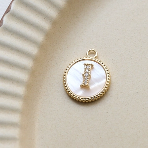 Macro view of gold plated round shell pendant with zircon letter I inlay detail