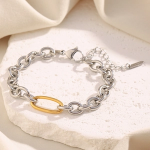 Detail of two-tone link bracelet with gold oval ring and lobster clasp on stone