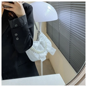 Chic white lace crossbody bag with large bow and pearl strap shown on shoulder