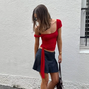 Detail of red square neck top with waist tie and dark grey pleated skirt set