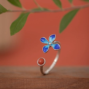 Macro view of adjustable silver ring with blue enamel flower and red gemstone detail