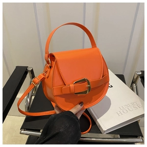 Orangefarbene PU-Satteltasche mit Goldschnalle auf schwarzem Stuhl und weißem Buchhintergrund