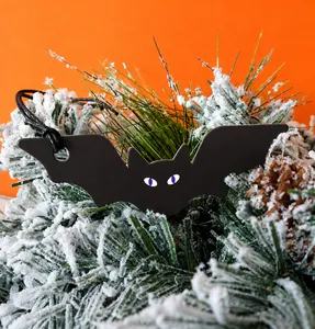 Cute black bat Halloween gift tag with purple eyes hanging on pine branch decor