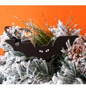 Cute black bat Halloween gift tag with purple eyes hanging on pine branch decor