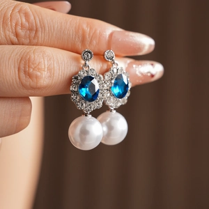 Dettaglio macro di orecchini vintage in argento con cristallo blu e perla bianca pendente