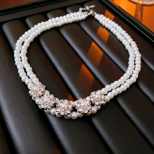 Macro detail of double-layered pearl necklace with rhinestone flower pendants and silver finish