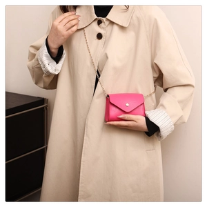 Close-up of rose red stone pattern small square bag with golden chain strap on beige coat