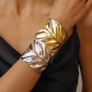 Macro shot of gold and silver metallic leaf textured wide cuff bracelets on model