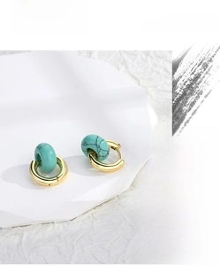 Detailed shot of vintage gold hoops with green turquoise stones on a white platform