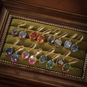 Close-up of geometric oval gemstone earrings in various colors set in a velvet wooden box