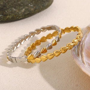 Detail of linked heart bracelets in gold and silver finish on natural stone background