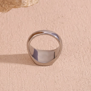 Close-up of polished silver stainless steel ring with flat top on textured beige stone
