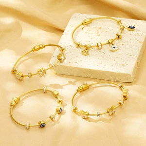 Detail of four gold-plated evil eye and butterfly charms on woven bangles over silk