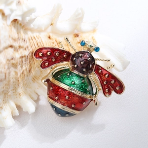 Detailed close-up of a gold honey bee brooch with red and green enamel on a white shell