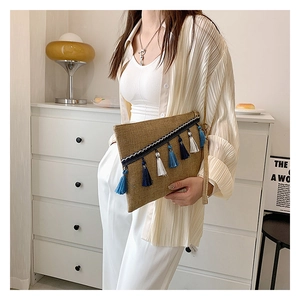 Detail of a brown woven envelope clutch bag with colorful tassels held by a model