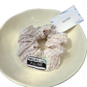 Plaid fabric scrunchie with brand label in a ceramic bowl, minimalist hair accessory