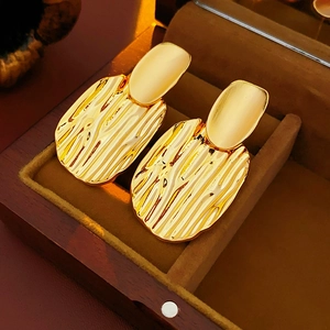 Détails de boucles d'oreilles dorées avec texture ondulée dans un écrin de luxe