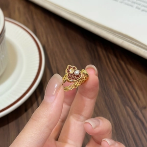 Nahaufnahme eines goldenen Gitterrings mit rotem Herzanhänger und Perlendetail