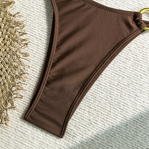 Détail du bas de bikini marron foncé avec anneaux métalliques dorés et coutures fines