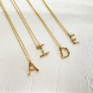 Detailed view of four 18k gold necklaces with colorful zircon letter pendants A, I, D, E