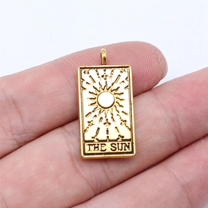Golden tarot 'The Sun' pendant charm on a finger showing its 26x13mm miniature size