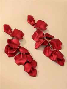 Détail de boucles d'oreilles pétales de rose rouges avec chaîne dorée sur fond beige
