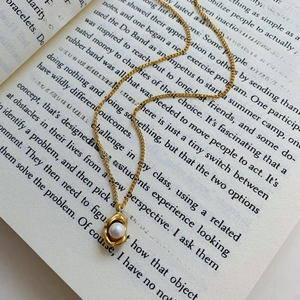 Elegant gold necklace with geometric pearl pendant resting on a vintage book page