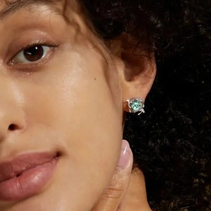 Close-up of a silver earring with a green round gemstone worn on a model ear