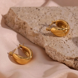 Close-up of golden streamlined hoop earring on beige stone and pink silk background