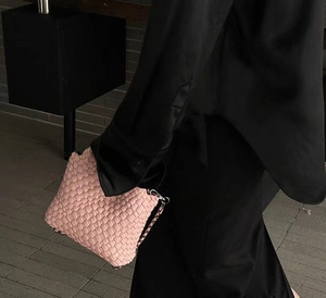 Detailed shot of pink woven bucket bag with metal chain strap carried by a model