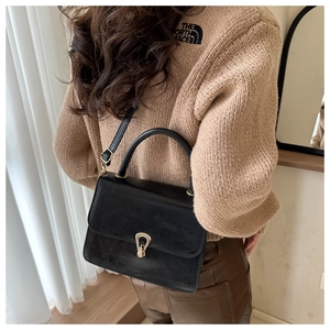 Detail of black leather handbag with gold lock and detachable strap on a model shoulder