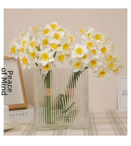 Detailed view of white faux narcissus with yellow centers in a fluted glass vase