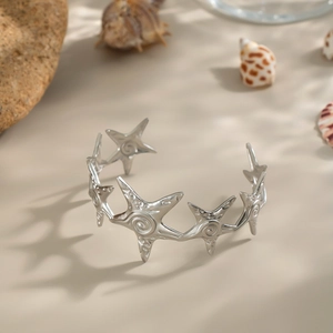 Macro shot of silver starfish textured open bangle set on sand with sea shells