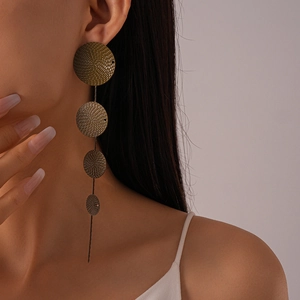 Close-up of golden geometric round textured long drop earrings on model’s ear