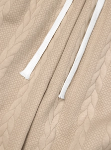 Detailaufnahme der beigen Zopfstrick-Textur und der weißen Baumwollkordel an der Hose