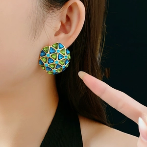 Close-up of vintage gold disc earrings with blue and green mosaic pattern on model