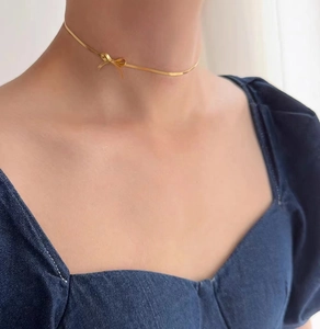 Close-up of a gold bow pendant necklace on a female model neck in soft natural lighting