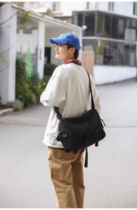 Outdoor street style shot of a black large canvas messenger bag with adjustable strap