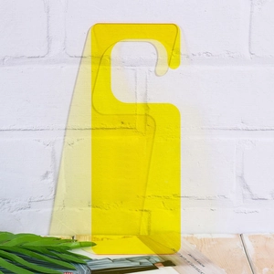 Clear yellow acrylic door hanger sign with minimalist design on white brick background