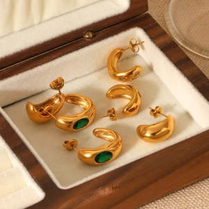 Detailed macro view of 18K gold C-shaped earrings with emerald and zircon in a jewelry box