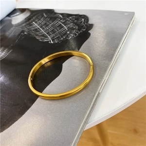 Minimalist oval 18K gold-plated stainless steel bangle with a satin finish on a white surface