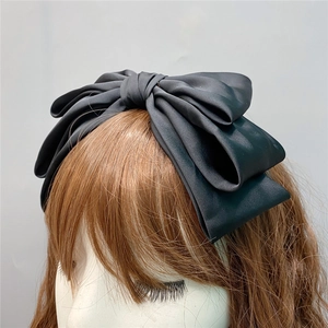 Detailed view of a multi-layer black satin oversized bow headband on a mannequin