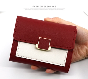 Détail du portefeuille bicolore rouge et crème avec boucle dorée tenu à la main