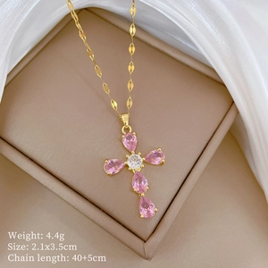 Golden cross necklace with pink drop gemstones displayed in a jewelry box with silk