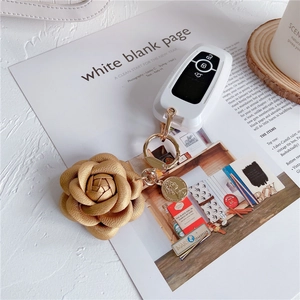 Detailed macro view of the gold leather camellia charm and white car key case on desk